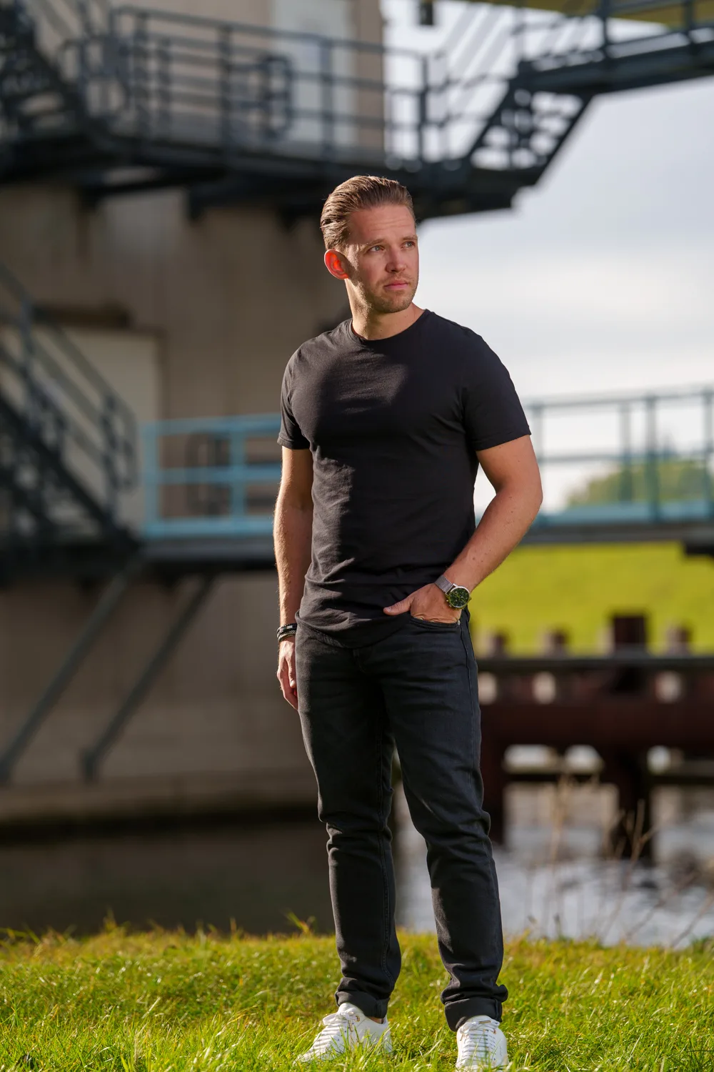 Man in zwart shirt poseert bij een industrieel hek