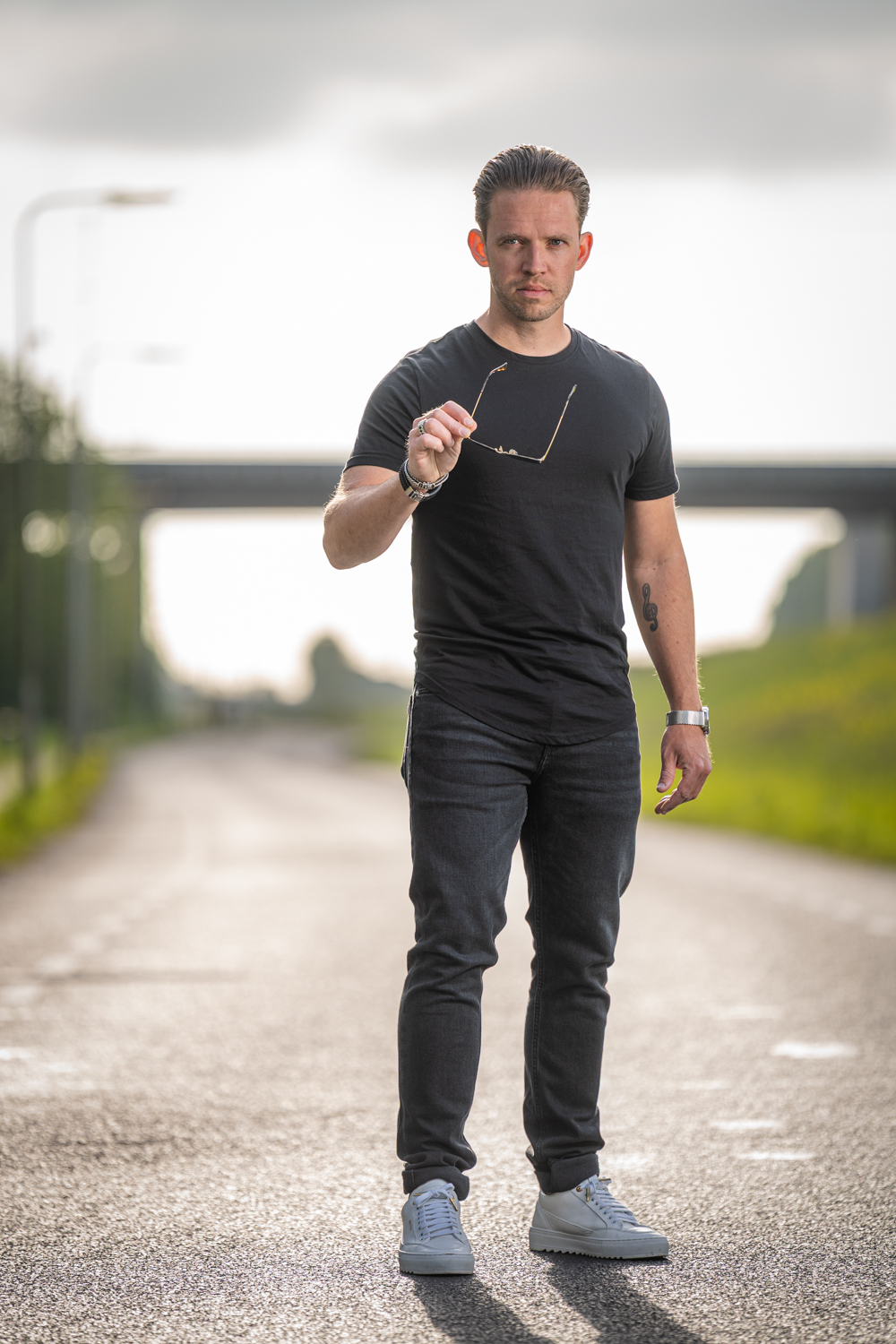 Man loopt zelfverzekerd op een weg met brug op de achtergrond