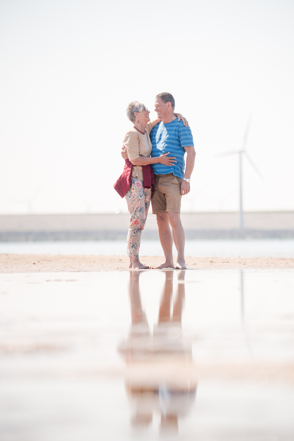 Ouder echtpaar omarmt elkaar op het strand met weerspiegeling in het water