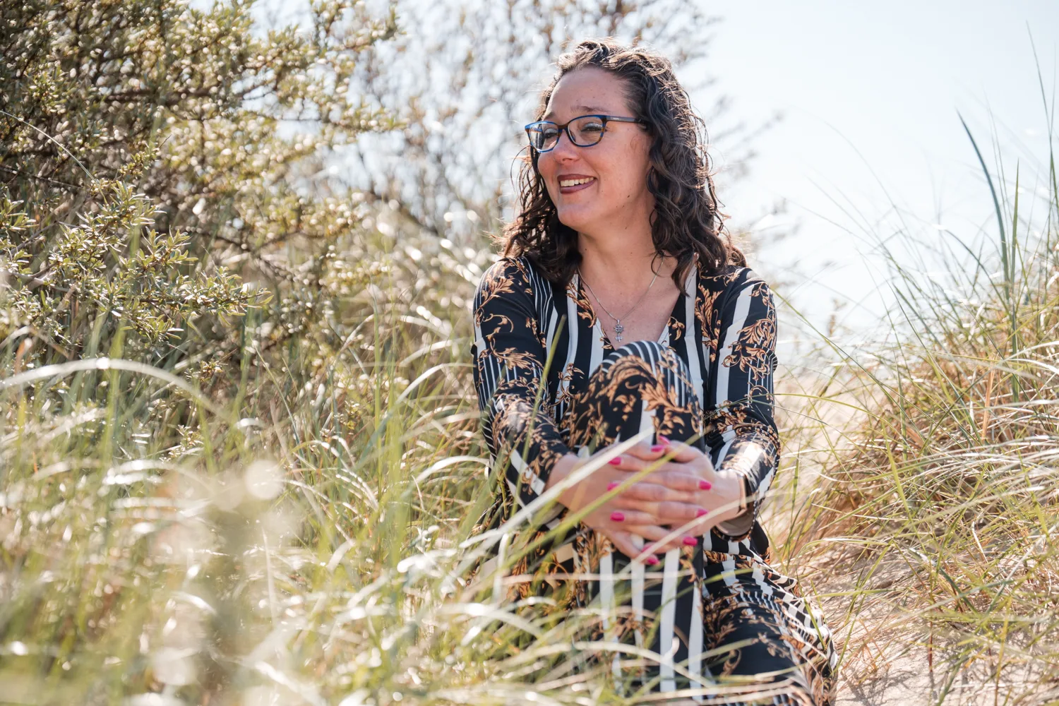 Vrouw met krullen zit lachend in het duingras