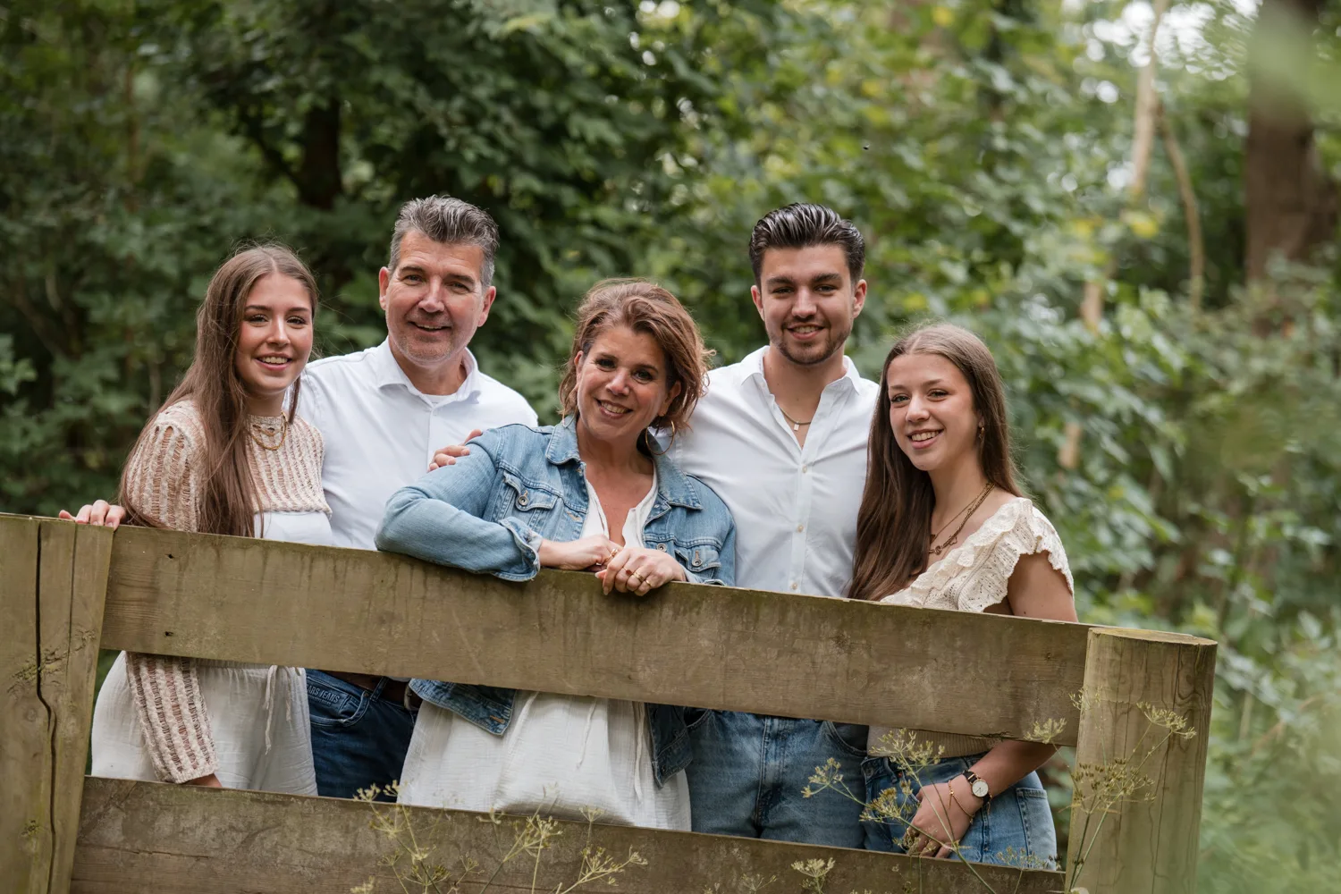Gezin van vijf leunend op een houten hek in het bos