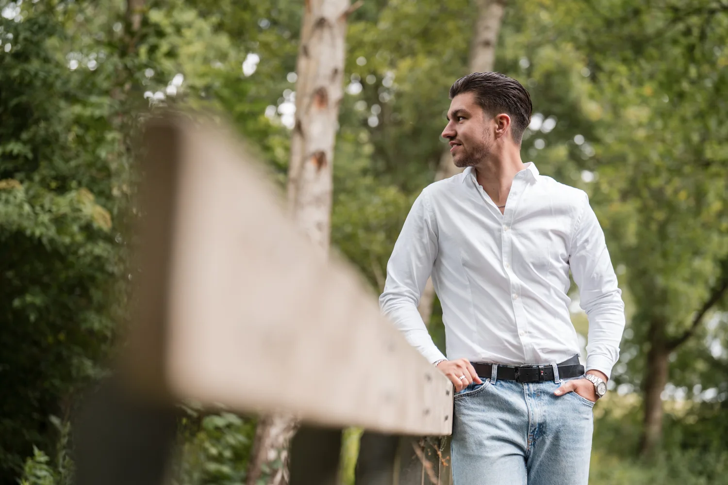 Man in wit overhemd leunt ontspannen tegen een hek in het groen