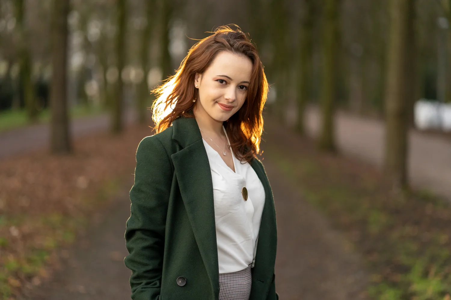 Jonge vrouw in groene jas op een bomenlaan in de herfst