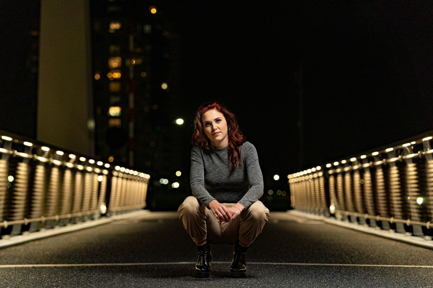 Portret van een vrouw gehurkt op een verlichte brug bij nacht