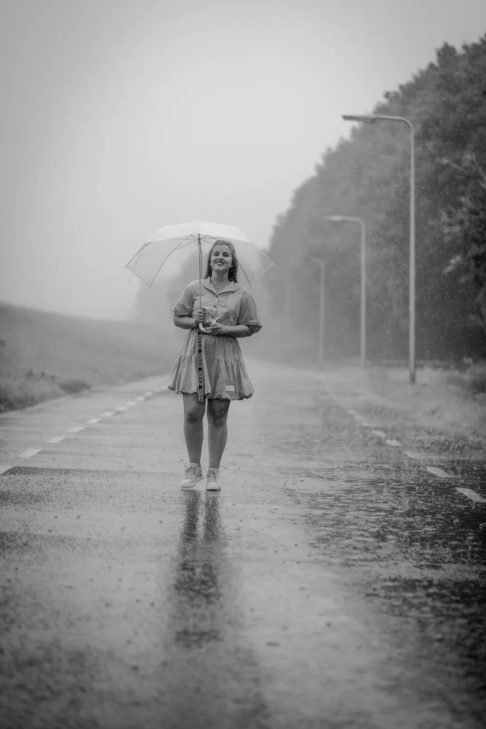 Jonge vrouw loopt lachend met paraplu in de regen, zwart-wit